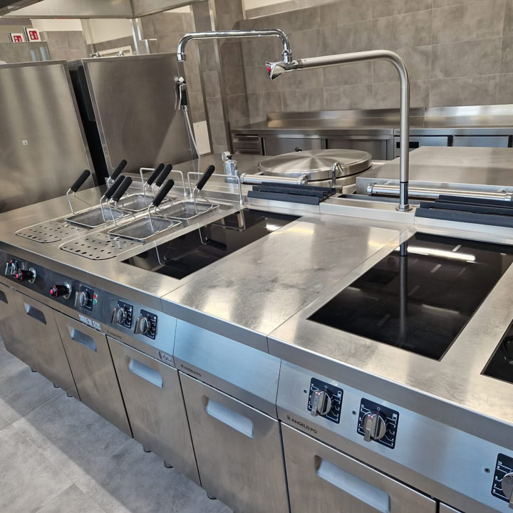 Sala da pranzo con tavoli, sedie e cucina di servizio sullo sfondo