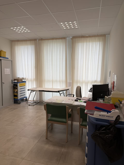 Studio medico con scrivania, lettino di visita e carrello presidi